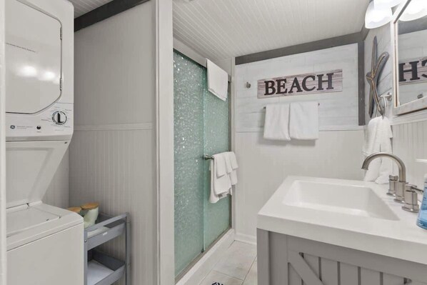 A bathroom with a white sink, a mirror, a towel rack, and a sign that reads "BEACH". - Reel Life - By Beach Access (Jekyll Island)