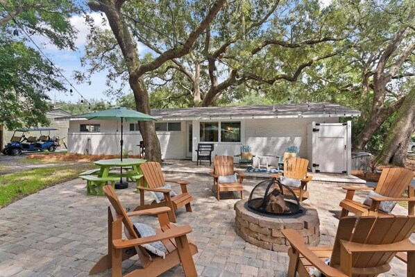 A patio area with wooden chairs, a green table, and a fire pit.