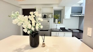 Una cocina moderna con armarios blancos, una isla central con un jarrón de flores blancas y dos lámparas colgantes.