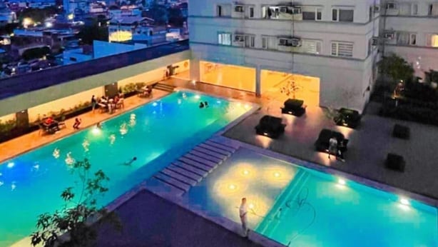 Un edificio de gran altura con piscina en la azotea, varios balcones y un paisaje urbano de fondo.