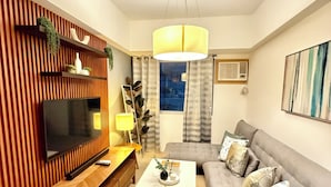 Una sala de estar moderna con un televisor de pantalla plana, un panel de pared de madera, un sofá gris y una lámpara colgante.