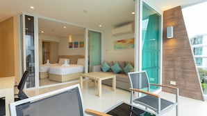 A modern hotel room with a large bed, a sofa, a desk, and a chair. There is a glass wall with a view of the outside. - Sea View Beach Dinning Beach Front c113 (Rawai)