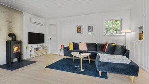A modern living room with a black wood-burning stove, a flat-screen TV, a dark blue sofa, and a coffee table.