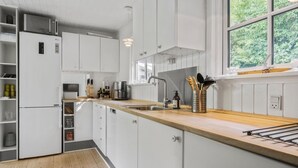 A modern kitchen with white cabinetry, a wooden countertop, and a window providing a view of greenery outside.