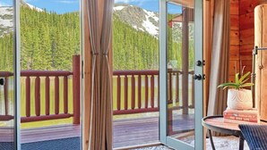 Eine Holzhütte mit Glastür, die auf eine Terrasse mit Blick auf einen Wald und Berge führt.