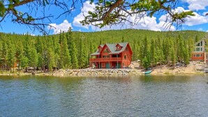 Eine rote Holzhütte an einem See, mit einem Wald im Hintergrund.