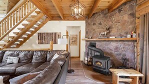 Ein gemütliches Wohnzimmer mit Kamin aus Stein, einer Ledersofa und einer Holztreppe.