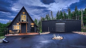 A modern cabin with a triangular roof, a large garage, and a paved driveway. - Aspen A-Frame Hot Tub Mountain Retreat Evergreen (Evergreen)