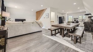 A modern living room with a sofa, a wooden dining table with benches, and a staircase leading to another level. - Aspen A-Frame Hot Tub Mountain Retreat Evergreen (Evergreen)