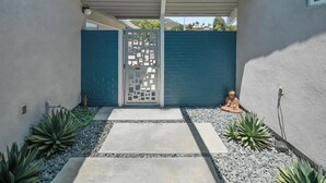 A modern outdoor entrance with a concrete pathway, a decorative gate, and a Buddha statue.