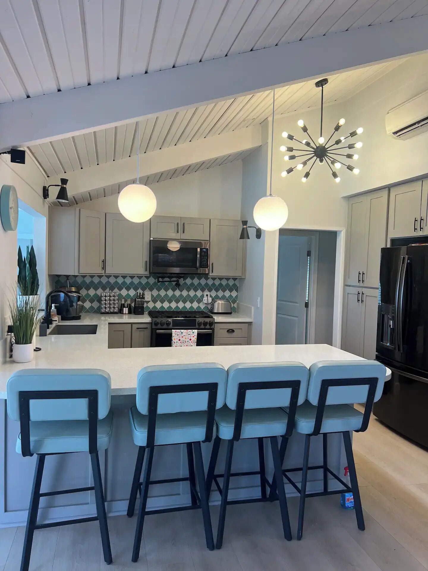 Une cuisine moderne dotée d’un îlot central, de tabourets de bar, d’appareils électroménagers en acier inoxydable et de luminaires suspendus.