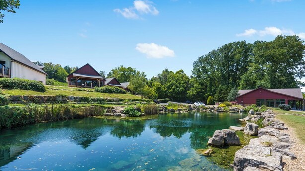 A serene lakeside setting with clear water, a stone pathway, and buildings with red roofs.