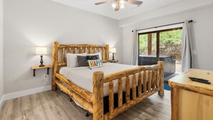 A wooden-framed bed with a pillow labeled "HAPPY" in a room with a ceiling fan, two bedside lamps, and a view of greenery outside.