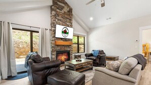 A living room with a stone fireplace, leather sofas, and a television mounted on the wall.