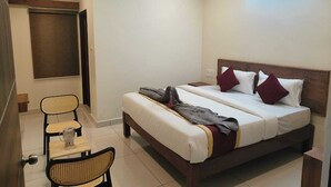 Una camera d'albergo con un letto, una sedia, un tavolino, una ventola a soffitto e una finestra con persiane.