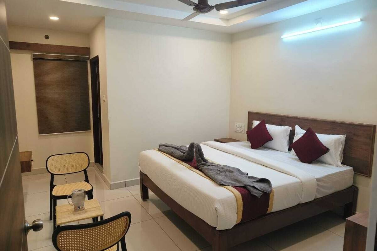 A hotel room with a bed, a chair, a small table, a ceiling fan, and a window with blinds.