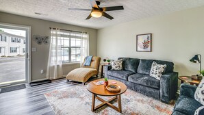 Ein Wohnzimmer mit Sofa, Sesseln, Couchtisch, Deckenventilator und Blick durch eine Tür.