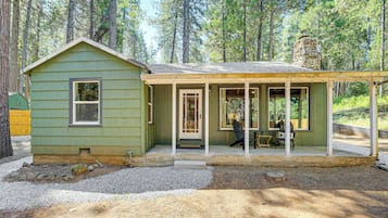 Situated in a forested area, this cabin features a covered porch with a bench, offering a tranquil outdoor space.