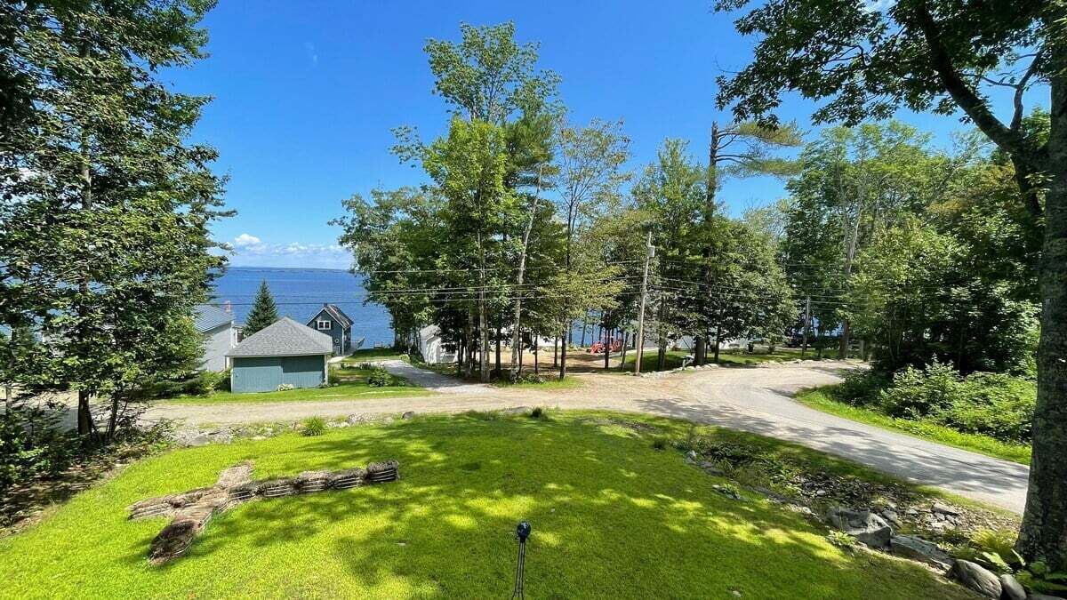 Une propriété résidentielle dotée d’une cour gazonnée, d’une terrasse en bois et d’une vue sur l’eau.