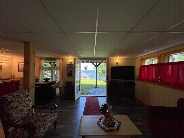 A spacious living area with a sofa, a coffee table, a television, and a view through the glass doors. - Slice of Heaven, steps to the beach (Northport)