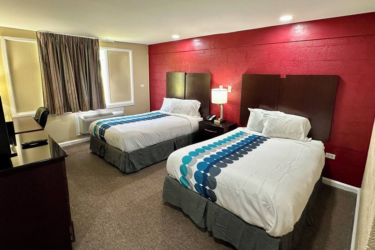 A hotel room with two beds, a desk, and a chair.