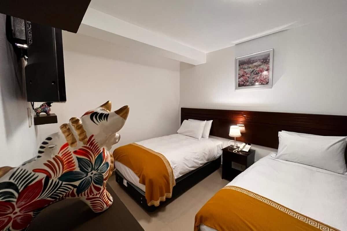 Una habitación de hotel con dos camas, una mesita de noche con lámpara, un televisor montado en la pared y una estatua decorativa de cebra.
