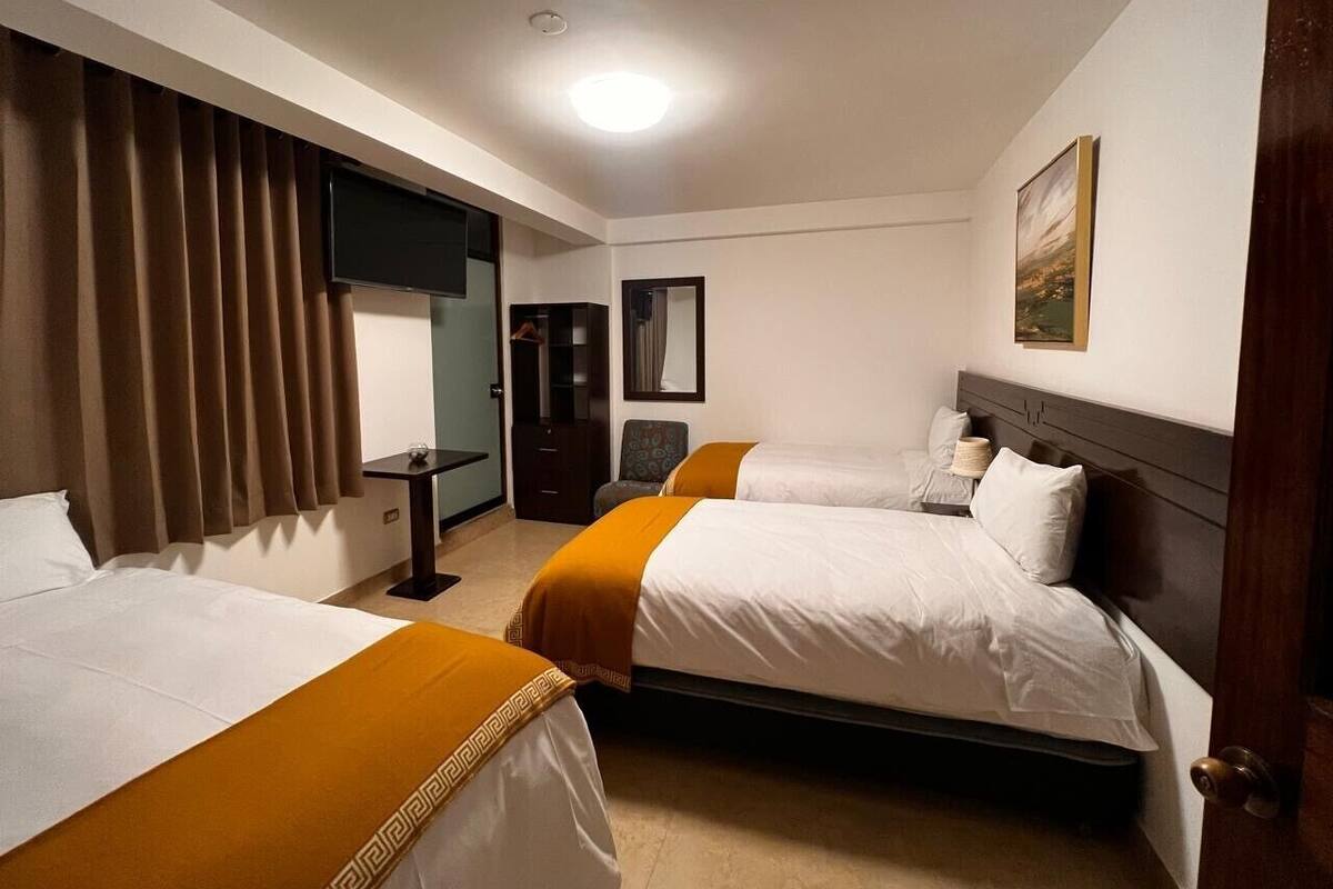 Habitación de hotel con dos camas, un escritorio, una silla, un armario y un cuadro en la pared.