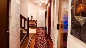 Un pasillo con suelo de madera, paredes de mármol, alfombra roja con estampado y un cuadro en la pared derecha.