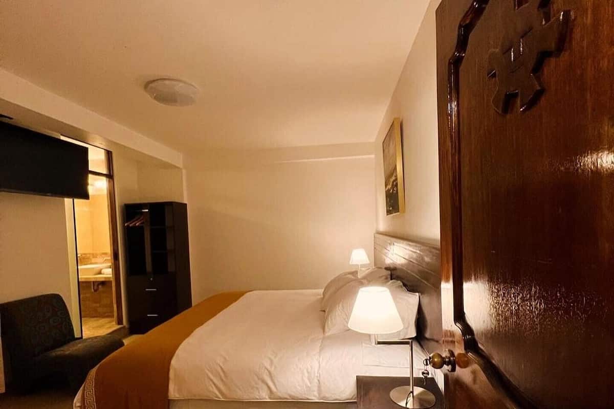 Una habitación de hotel con cama, lámpara de noche, cómoda y una silla.