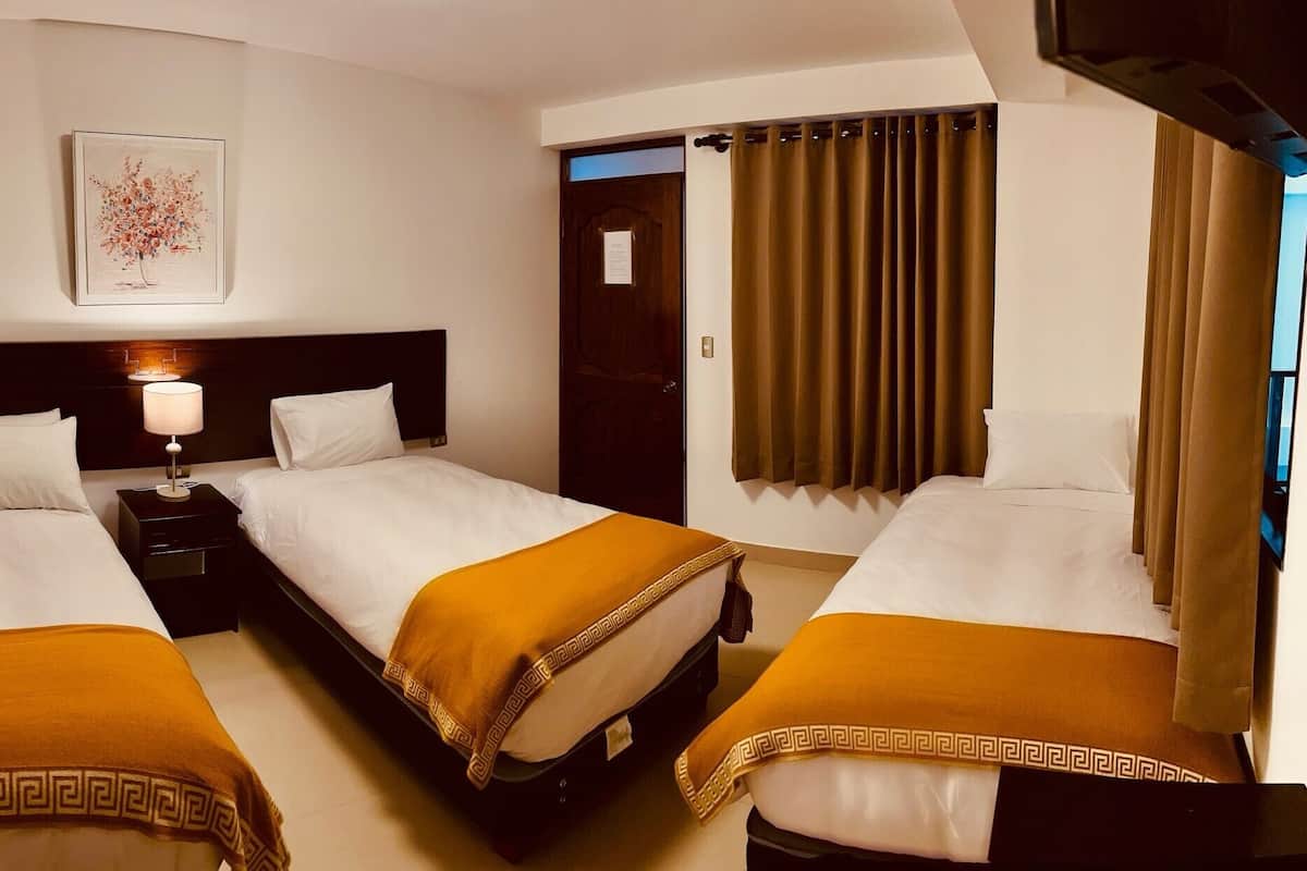 Habitación de hotel con tres camas, una mesita de noche con lámpara, un cuadro en la pared y una puerta con cortinas.