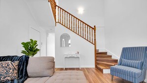 A living room with a sofa, ottoman, and armchair, a staircase, and a white console table.