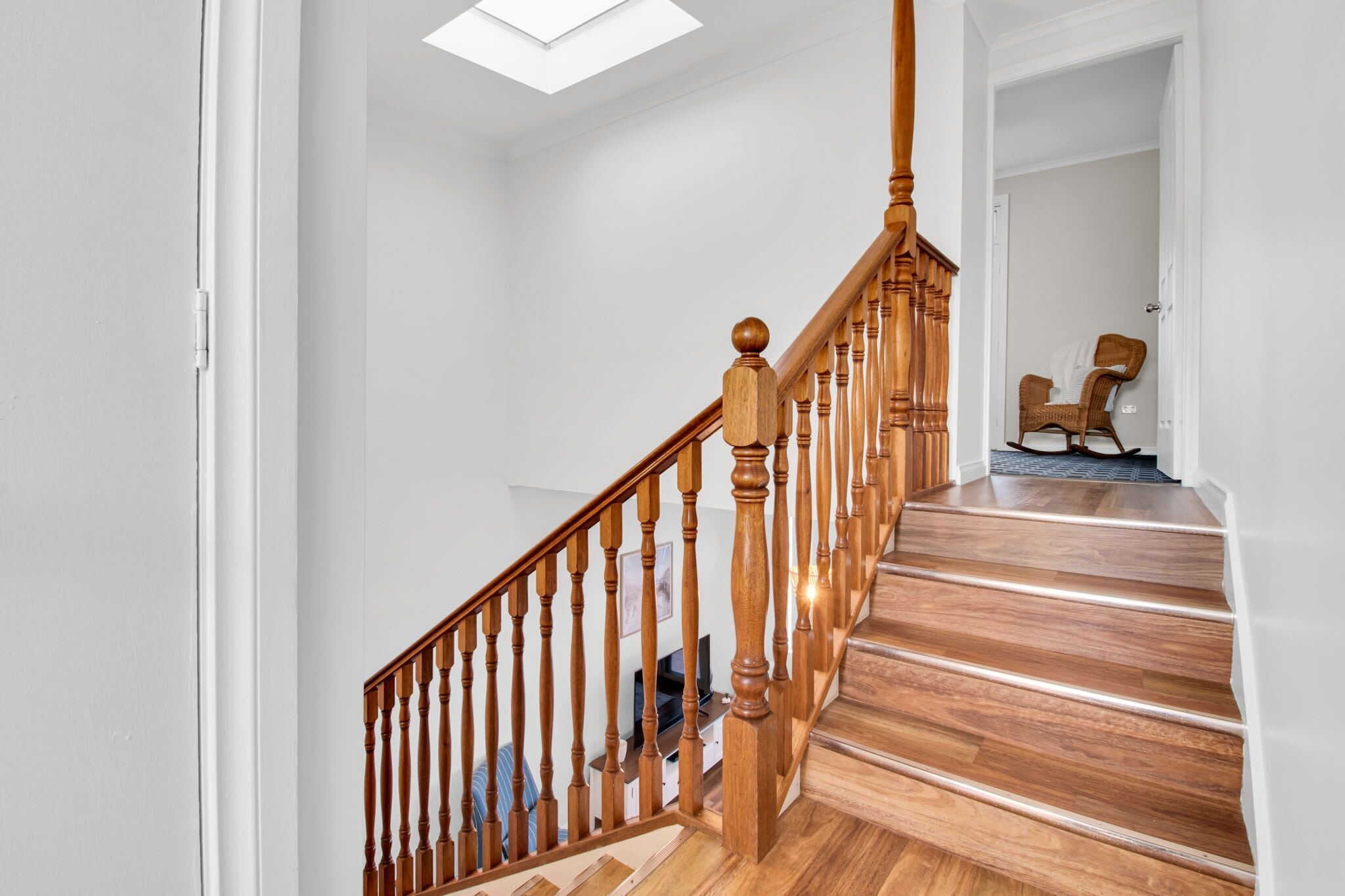 A staircase with wooden balusters and a handrail, leading to a landing with a chair and a television.