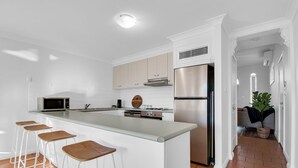 A modern kitchen with white cabinetry, a stainless steel refrigerator, and a bar stool area.
