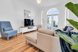 Una sala de estar con sofá, una silla, televisor y una planta grande.