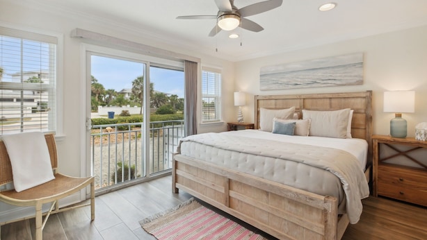 A bedroom with a large bed, a ceiling fan, a view through the glass door, and a wooden nightstand. - Amelia Sunrise - Oceanview, Bikes, & Beach Access (Fernandina Beach)