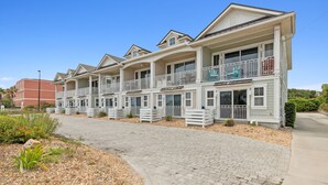 A row of two-story townhouses with balconies, a paved driveway, and a landscaped garden area. - Amelia Sunrise - Oceanview, Bikes, & Beach Access (Fernandina Beach)
