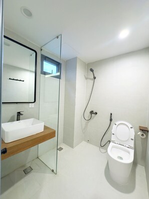 Een moderne badkamer met een glazen douchecabine, een wit wastafelmeubel met houten blad en een toilet met papierhanddoekhouder.