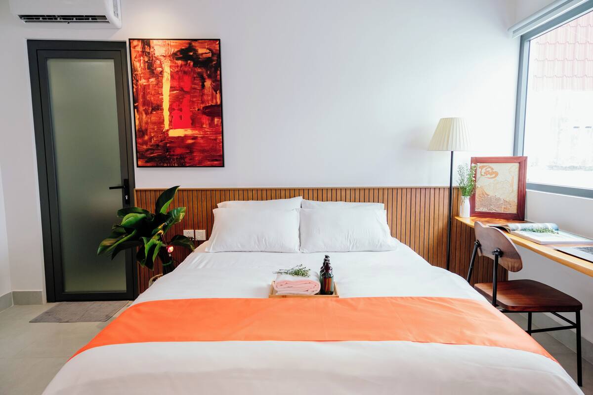 Une chambre d’hôtel avec un lit, un bureau, une chaise, une plante et un tableau au mur.