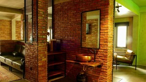 A room with a brick wall, a large mirror, a copper sink, a leather sofa, and a window. - Urban Hotel (Ho Chi Minh City)