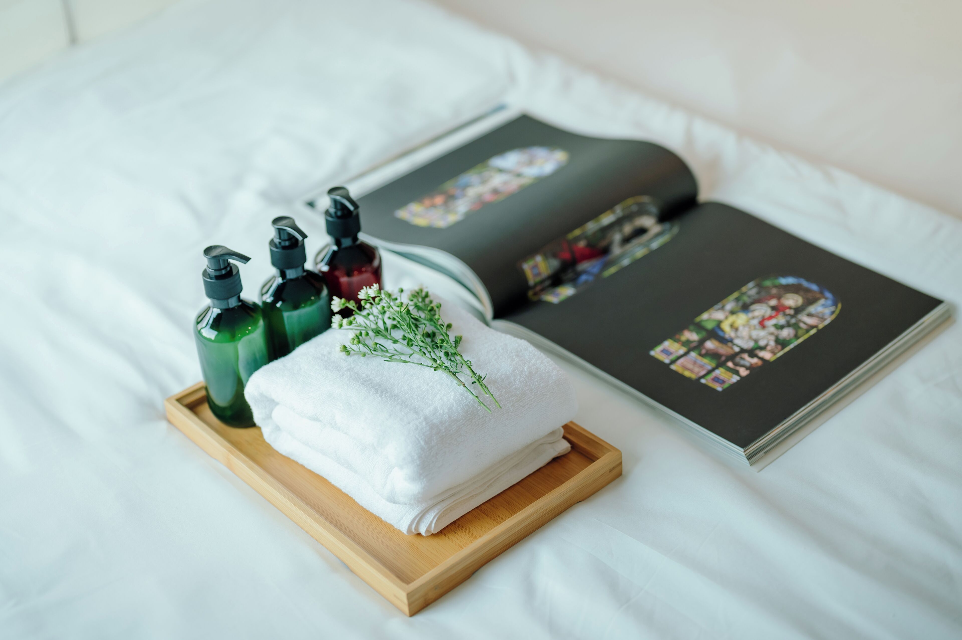 A neatly arranged bathroom with a white towel, green and red bottles, and a book on a wooden tray.