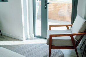 A modern room with a wooden chair, a glass door leading outside, and a light-colored rug on the floor. - Urban Hotel (Ho Chi Minh City)