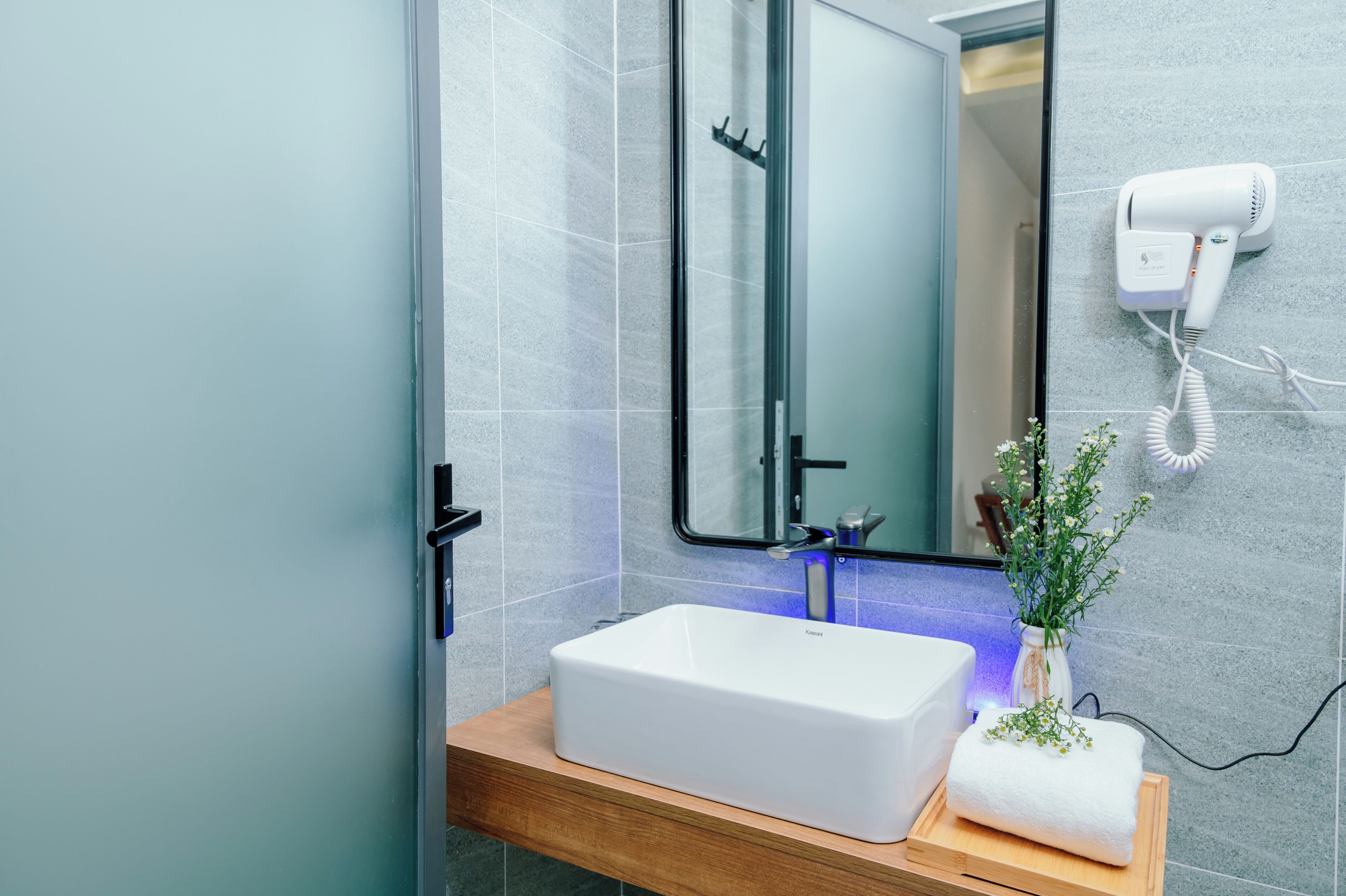A modern bathroom with a white sink, a mirror, and a hair dryer mounted on the wall.