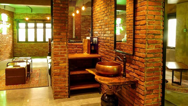 A bathroom with a brick wall, a wooden vanity, a large mirror, and a hanging light fixture. - Urban Hotel (Ho Chi Minh City)