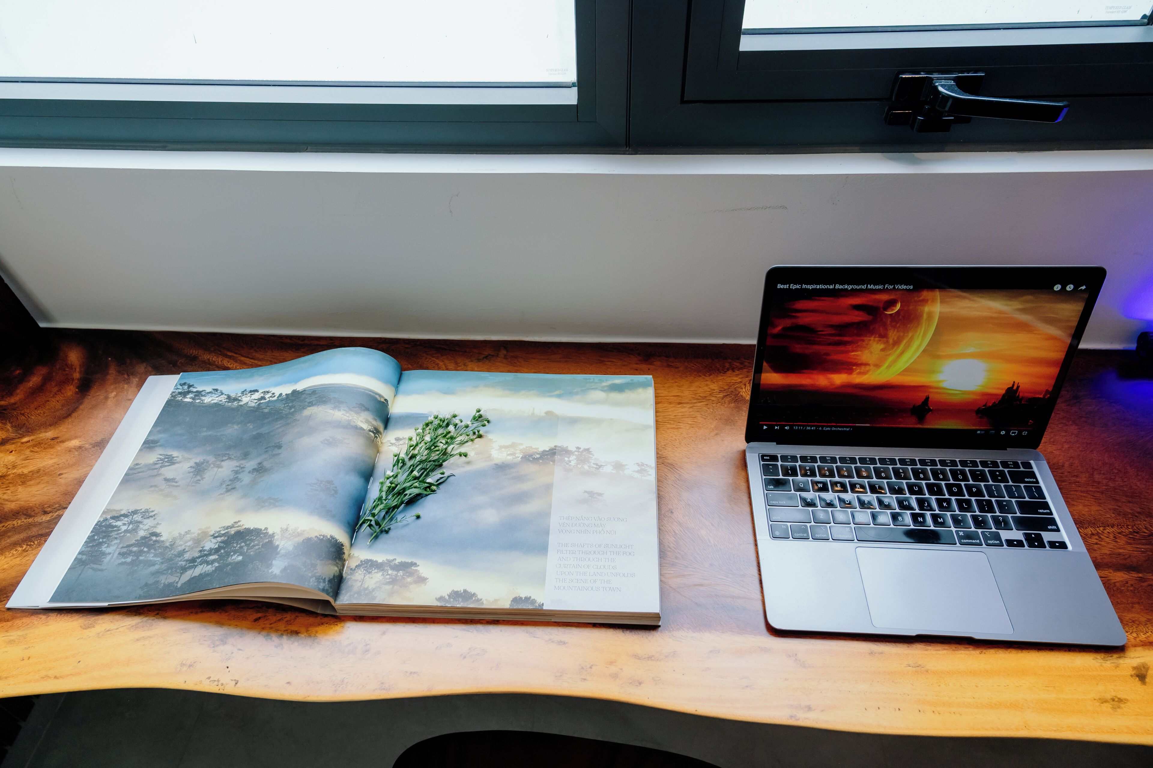 A laptop on a wooden desk with a book beside it.
