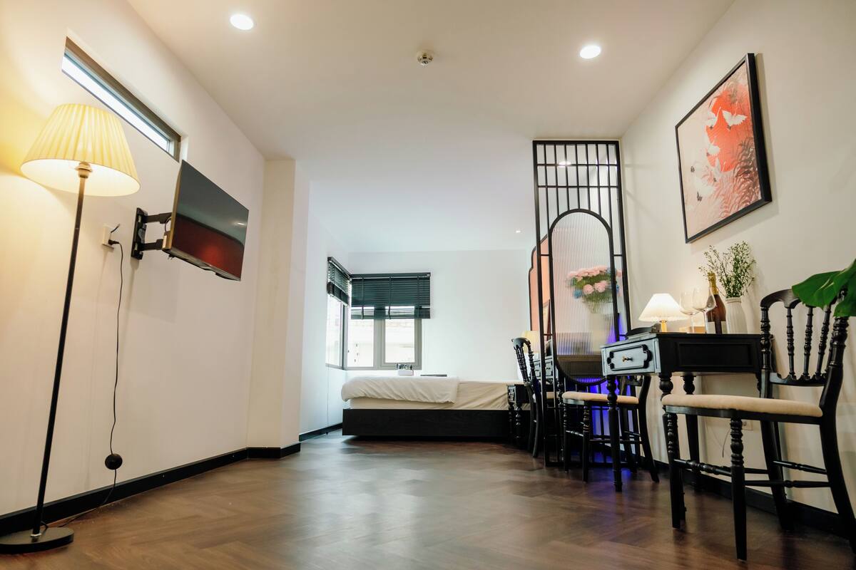 Une chambre moderne avec un lit, un téléviseur fixé au mur, un bureau avec une chaise et une fenêtre avec des stores.