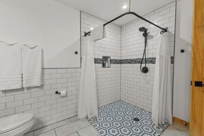 Un baño moderno con azulejos blancos tipo metro, una ducha con cabezal de ducha tipo lluvia negro y un piso con diseño.