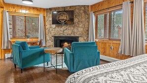 Una habitación acogedora con chimenea de piedra, sillones color turquesa, una cama con ropa de cama estampada y un televisor en la pared mostrando 'elevate bnb'.