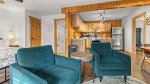 Una cocina moderna con armarios de madera, un refrigerador de acero inoxidable y un comedor con sillas color turquesa y una mesa redonda pequeña.