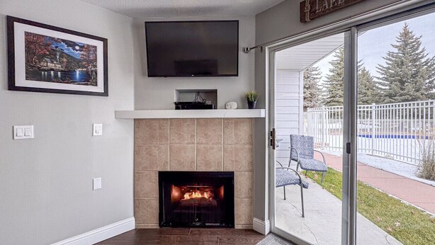 A living room with a fireplace, a flat-screen TV mounted above it, and a sliding glass door leading to an outdoor area. - Inn Building Condo #107, ground level, pool view (Garden City)