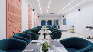 A modern dining area with teal chairs and tables, geometric wall decor, and a long view towards a blue-lit wall. - Treebo Premium Aasma Courtyard (Kujang)